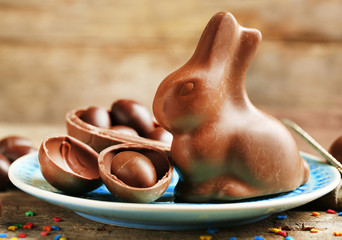 Chocolate Easter eggs and rabbit on plate, on wooden background