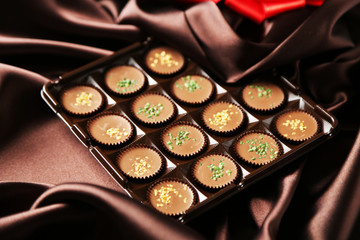 Tasty chocolate candies on satin cloth, close up