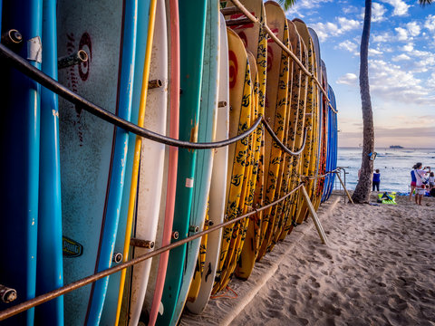Colourful surfboards stacked up on Waikiki Beach at sunset.