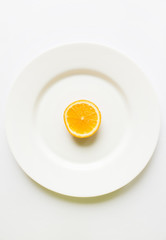 One half of sliced orange on a white round plate on a white back