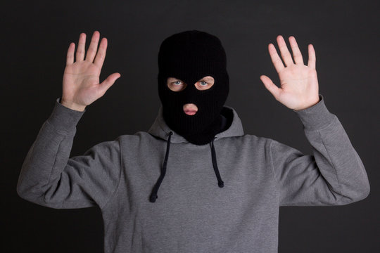 man in black mask holding hands up over grey