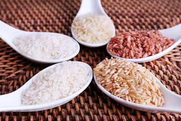 Different types of rice in spoons on wicker background