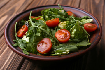 Salad with arugula and cherry tomatoes on wooden table
