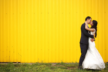 Bride and Groom kissing against yellow wall