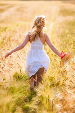 Happy young blonde girl in white dress with straw hat running th