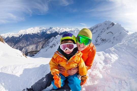 Little skier, father sit in snow on mountain peak
