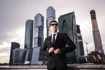 Businessman buttons his jacket on the background of skyscrapers.