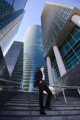 Businessman standing on a ladder, surrounded by skyscrapers.
