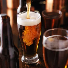 Crédence de cuisine en verre imprimé Bière verser de la bière dans un verre sur une table en bois