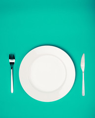 white plate, fork and knife on emerald background