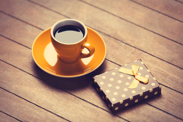 Cup of coffee and gift box on a wooden table.