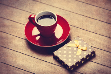 Cup of coffee and gift box on a wooden table.