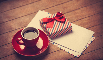 Cup of coffee and gift box with envelopes on a wooden table.