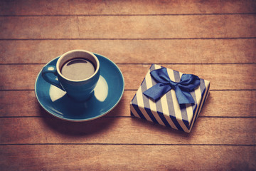 Cup of coffee and gift box on a wooden table.