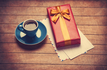 Cup of coffee and gift box with envelopes on a wooden table.