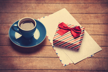 Cup of coffee and gift box with envelopes on a wooden table.