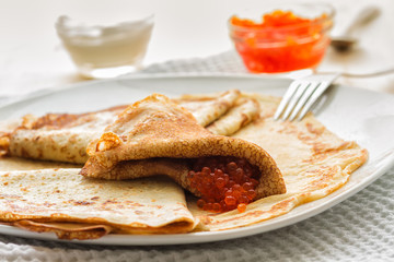 plate of pancakes, red caviar, sour cream on a wooden table