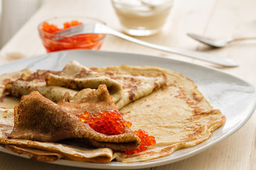 plate with pancakes and red caviar on a wooden table
