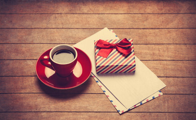 Cup of coffee and gift box with envelopes on a wooden table.