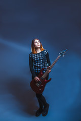 European-looking girl in a sweater holding a guitar and looking