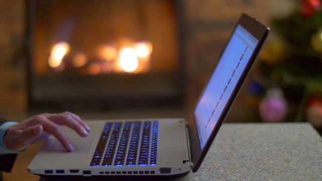 The man work with laptop - type text. By fireplace background