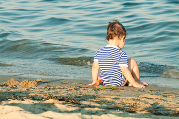 Fototapeta na wymiar Adorable toddler with sailor shirt sitting at the edge of the wa