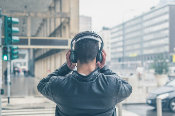 Back view of a young man with headphones posing in the city stre