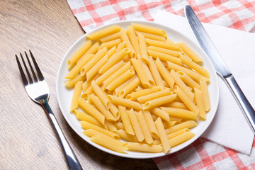 close up of raw italian pasta in plate with fork and knife