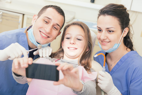 Happy patient, dentist and assistant taking selfie all together