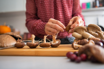 Closeup on young housewife stringing mushrooms on string