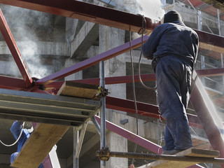 Welder with protective helmet welding metal on construction site