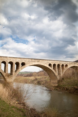Fototapeta premium Old stone middle age bridge in Bulgaria, against a cloudy sky