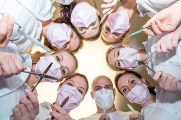 A team of dentists with tools and masks bending over patient - obrazy, fototapety, plakaty