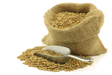 green dried lentils in a burlap bag on a white background