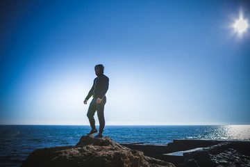 Man stands on a rock by the sea against the sky