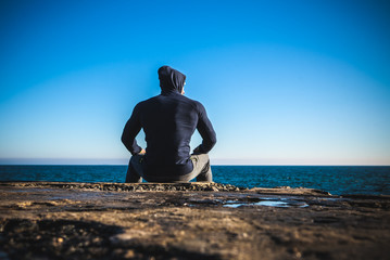 athlete taking break sitting on rocks with sea horizon