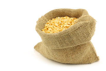 yellow split peas in a burlap bag on a white background