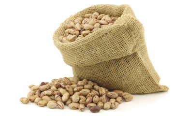 speckled beans in a burlap bag on a white background