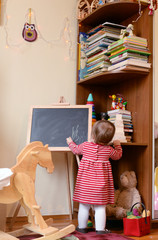 Small girl in a dress drawing on a chalkboard