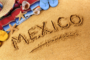 Fototapeta na wymiar Mexico beach writing word written in sand on a mexican beach with sombrero and accessories photo