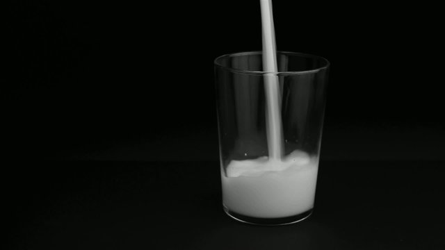 Milk pour into a glass, black background