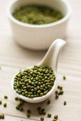 Raw mung beans in ceramic spoon over white wooden background