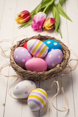 Fresh tulips and colorful easter eggs in a nest on a wooden tabl