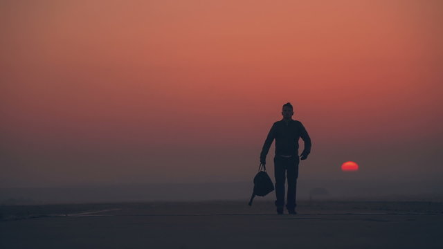 A man leaves the sunrise with a bag