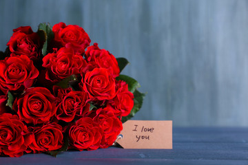 Bouquet of red roses with tag on wooden background