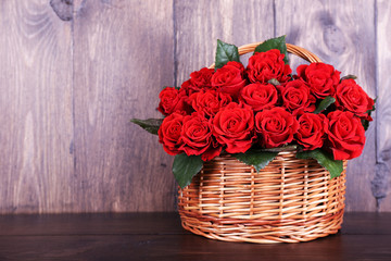 Fototapeta na wymiar Bouquet of red roses in basket on wooden background