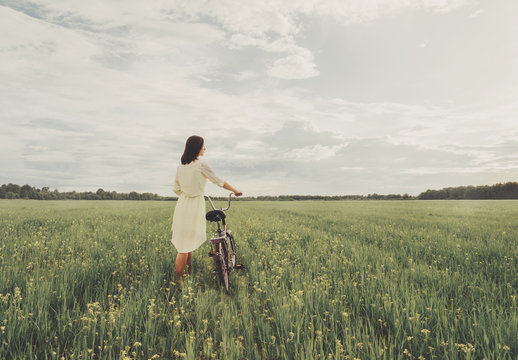 Young woman walking with a bicycle on summer meadow