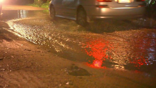 Car  and motorbike drives through a puddle on the road at night