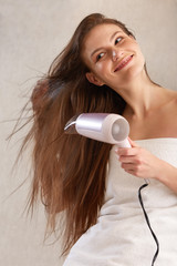 Hair. Young woman blow drying hair in bathroom