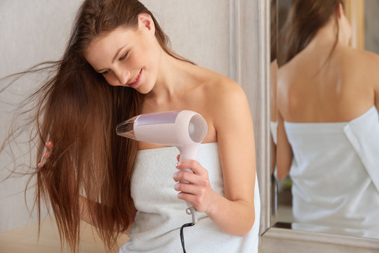 Hair. Young Woman Blow Drying Hair In Bathroom